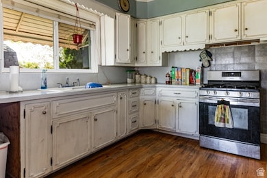 Kitchen with gas stove, light countertops, dark wood-style flooring, backsplash, and pendant lighting
