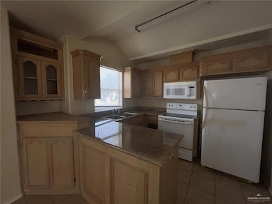 Kitchen with white appliances, a peninsula, light tile patterned flooring, lofted ceiling, and light brown cabinets