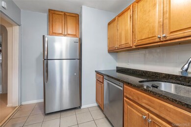 Kitchen featuring brown cabinetry, stainless steel appliances, dark stone countertops, tasteful backsplash, and arched walkways
