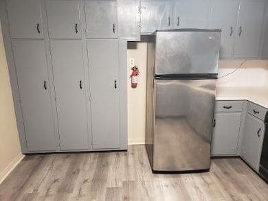 Kitchen with freestanding refrigerator, gray cabinetry, light wood-style floors, baseboards, and light countertops