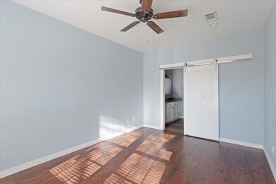 Unfurnished bedroom featuring dark wood-type flooring, visible vents, baseboards, and a barn door