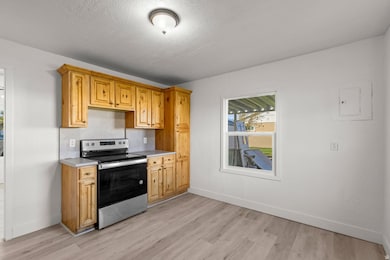 Kitchen with electric stove, light countertops, light wood-type flooring, a textured ceiling, and electric panel