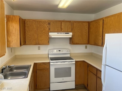 Kitchen featuring white appliances, light countertops, brown cabinetry, under cabinet range hood, and light wood finished floors