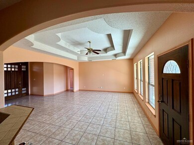 Living room with a textured ceiling, ceiling fan, light tile floors, and a raised ceiling