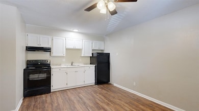Kitchen with black appliances, dark wood-style floors, white cabinets, under cabinet range hood, and light countertops