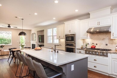 The light-filled gourmet kitchen featuring a sleek marble island and countertops, a Thermador 6-burner cooktop, oven, built-in microwave, Bosch dishwasher, and walk-in pantry.