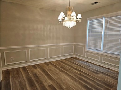 Unfurnished dining area featuring a chandelier, a decorative wall, dark wood-type flooring, and a wainscoted wall