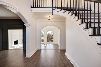 Entrance foyer with arched walkways, crown molding, wood finished floors, a fireplace with raised hearth, and a high ceiling