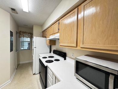 Kitchen with stainless steel microwave, electric range, under cabinet range hood, light brown cabinetry, and light countertops