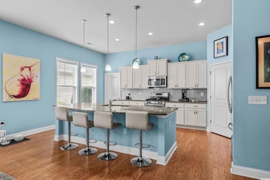 Kitchen featuring stainless steel appliances, light wood-style floors, a kitchen bar, decorative backsplash, and white cabinetry