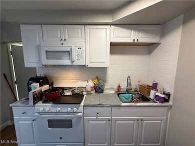 Kitchen featuring decorative backsplash, white cabinets, white appliances, and light countertops