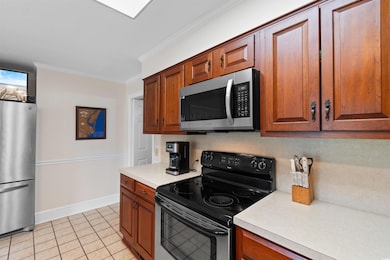 Kitchen featuring stainless steel appliances, crown molding, light countertops, light tile patterned floors, and brown cabinets