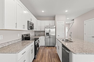 Kitchen with dark hardwood / wood-style flooring, white cabinets, sink, appliances with stainless steel finishes, and a kitchen island with sink