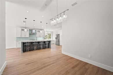Kitchen with stainless steel fridge, white cabinets, a breakfast bar, light wood-type flooring, and wall chimney range hood