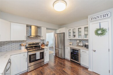 Kitchen with dark hardwood / wood-style flooring, wall chimney exhaust hood, wine cooler, white cabinetry, and stainless steel appliances