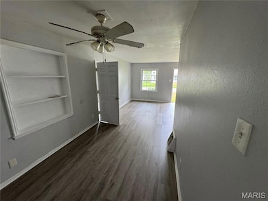 Unfurnished living room with dark wood-style floors, built in shelves, and a ceiling fan