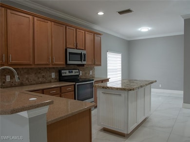 Kitchen featuring light marble finish floors, crown molding, stainless steel appliances, decorative backsplash, and light stone counters