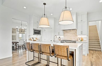 Kitchen featuring a kitchen bar, light stone countertops, white cabinets, light wood-style floors, and a center island with sink