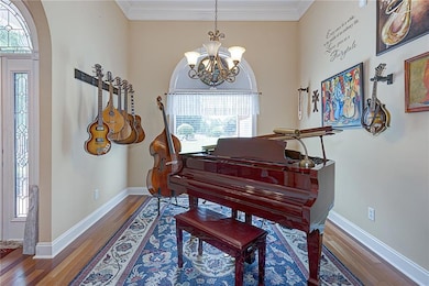 Sitting room with wood finished floors, a chandelier, crown molding, baseboards, and arched walkways