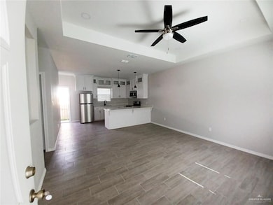 Unfurnished living room featuring a raised ceiling, ceiling fan, and wood finish floors
