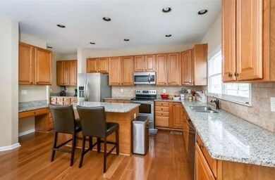 Kitchen with appliances with stainless steel finishes, light wood finished floors, a breakfast bar area, light stone counters, and a kitchen island