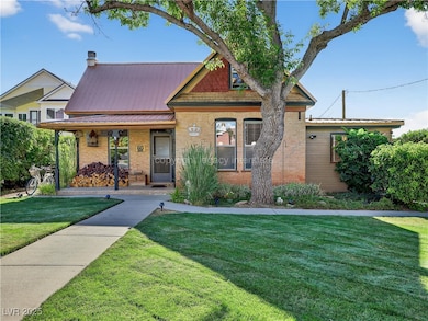 View of front facade featuring brick siding, a metal roof, a front lawn, and covered porch