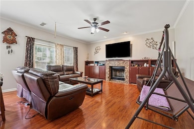 Living area featuring a ceiling fan, crown molding, wood finished floors, a tiled fireplace, and baseboards