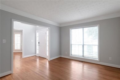 Spare room with plenty of natural light, crown molding, a textured ceiling, light wood-style floors, and baseboards