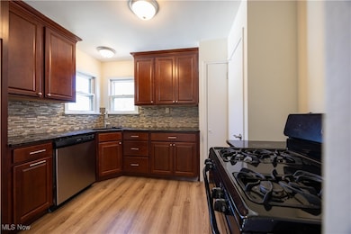 Kitchen featuring black gas stove, stainless steel dishwasher, light wood-style floors, backsplash, and dark stone counters