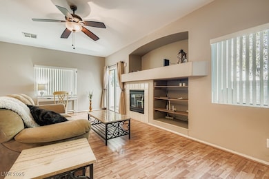 Living area with a tiled fireplace, light wood-type flooring, a ceiling fan, and built in features
