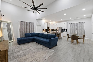 Living room featuring recessed lighting, light wood-style floors, ceiling fan, and a towering ceiling