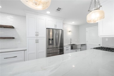Kitchen with light stone counters, white cabinetry, stainless steel appliances, and recessed lighting