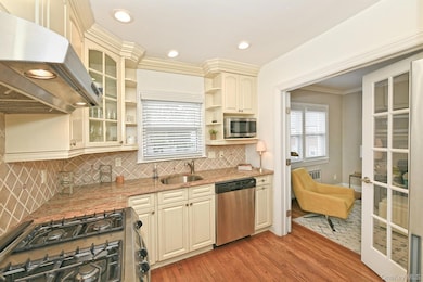 Kitchen featuring backsplash, under cabinet range hood, glass insert cabinets, stainless steel appliances, and cream cabinetry
