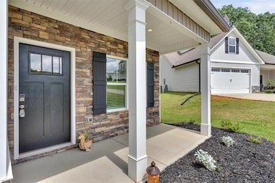 View of exterior entry with stone siding, covered porch, board and batten siding, a lawn, and a garage