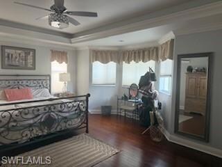 Bedroom with dark wood-type flooring, ornamental molding, ceiling fan, and a raised ceiling