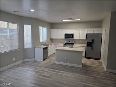 Kitchen with appliances with stainless steel finishes, white cabinets, light countertops, a center island, and light wood-style flooring