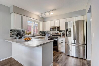 The sunlit kitchen provides an abundance of storage and counter space, breakfast bar seating, and tile backsplash.