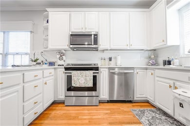 Kitchen featuring white cabinetry, appliances with stainless steel finishes, light wood-style floors, open shelves, and light stone counters