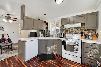 Kitchen featuring gray cabinets, white appliances, light countertops, dark wood finished floors, and decorative backsplash