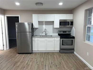 Kitchen with stainless steel appliances, backsplash, white cabinetry, light wood finished floors, and recessed lighting