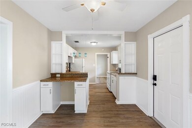 Kitchen with white cabinetry, a wainscoted wall, dark countertops, white appliances, and pendant lighting
