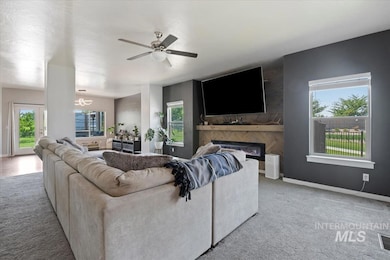 Carpeted living area featuring plenty of natural light, a glass covered fireplace, ceiling fan, and a chandelier