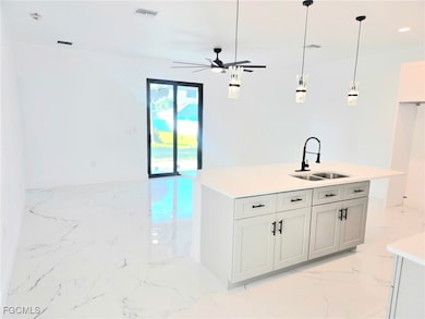 Kitchen featuring light marble finish flooring, a kitchen island with sink, hanging light fixtures, a ceiling fan, and light stone countertops