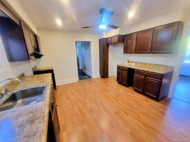 Kitchen with light countertops, light wood-type flooring, dark brown cabinets, and ceiling fan