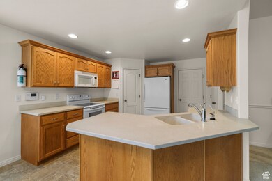 Kitchen featuring a peninsula, white appliances, brown cabinetry, and recessed lighting
