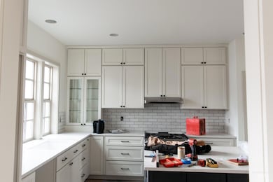 Kitchen with white cabinets, glass insert cabinets, decorative backsplash, recessed lighting, and under cabinet range hood