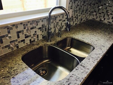 Kitchen view of a sink, backsplash, and stone countertops
