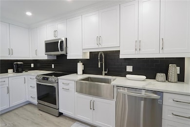 Kitchen with appliances with stainless steel finishes, a sink, white cabinetry, light wood-type flooring, and recessed lighting