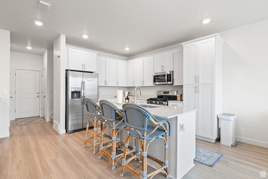 Kitchen featuring stainless steel appliances, white cabinets, a center island with sink, light stone counters, and light wood-style flooring