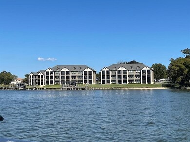 This photo shows a waterfront property with modern, multi-story buildings featuring large windows and balconies. The buildings are situated near a calm body of water, offering scenic views and potential for outdoor activities. The area appears tranquil and inviting, ideal for those seeking a serene lakeside lifestyle.